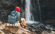 © Soloviova Liudmyla - Woman with a backpack in a red hat dressed in active trekking clothes sitting near the mountain river waterfall and enjoying the splashing Nature power. Traveling, trekking, and a nature concept image
