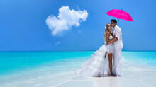 Summer Love. Beautiful Happy Young Couple In Wedding Clothes And Pink Umbrella Is Standing On A Beach In The Maldives. Engagements And Wedding On The Beach On The Maldives. 