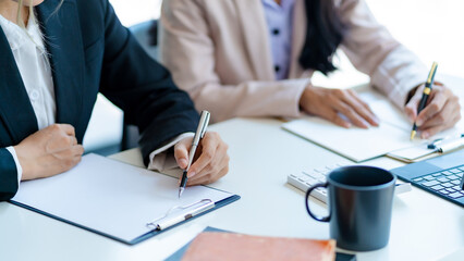 Close-up of business people taking note at a meeting on clipboard for drafting, writing meeting minutes in office and printing on computer.