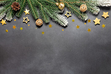 Creative Christmas and New Year composition with fir tree branches and golden decorations on black stone background with copy space for your design. 