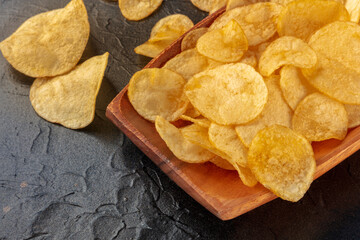 Poster - Potato chips or crisps in a bowl and scattered on a black stone background, a close-up with copy space