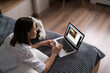 © arthurhidden - Young woman sitting on the bed wearing pajamas, with pleasure enjoying white flowers, chatting using laptop