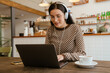 Leinwandbild Motiv White woman in headphones smiling and working with laptop at cafe