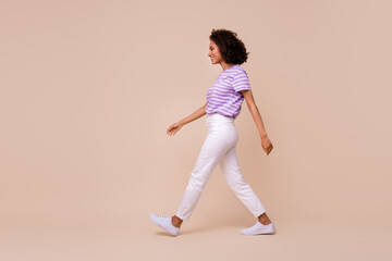 Wall Mural - Photo of shiny cute girl dressed purple t-shirt walking empty space isolated beige color background