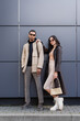 Leinwandbild Motiv full length of stylish interracial couple in autumnal outfits and trendy sunglasses standing near building.