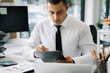 © NINENII - Businessman sitting at a table at home working on a laptop and writing down ideas in a tablet.