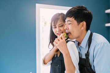 Wall Mural - Happy Asian couple cooking healthy food. attractive wife and cheerful husband preparing delightful meal with fresh ingredients. fun married people make vegetable salad for dinner together in kitchen