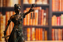 Lawyer Office. Statue Of Justice With Scales Close-up Against The Backdrop Of A Wall Of Books Or A Library . Legal Law, Advice And Justice Concept