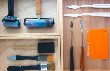 Art and craft DIY tools box. Rubber roller, foam brush, knife palette and paint brush on wooden tray.