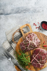 Steaks Raw. Raw cowboy steak, marbled beef meat with spices rosemary and pepper on old wooden board on old grey slate table background. Top view. Mock up.