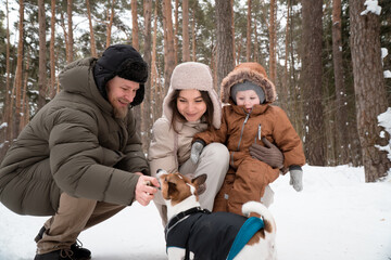 Family (mom,dad and baby) walking in winter forest with dog jack russell terrier