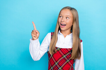 Wall Mural - Portrait photo of little cute positive schoolgirl kid look directing finger pointing empty space excited new college isolated on blue color background