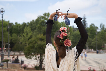 Wall Mural - Portrait of young teenage girl in black dance dress, white shawl and pink carnations in her hair, dancing flamenco with castanets in her hands. Concept of flamenco, dance, art, typical Spanish dance.