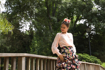 Canvas Print - Young teenage woman in pink shirt, black skirt with flowers and pink carnations in her hair, dancing flamenco on wooden bridge. Flamenco concept, dance, art, typical Spanish dance.