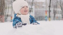 Cheerful Child Makes Snowman Outside During Snowfall. Joyful Small Child Sculpts Snowball.