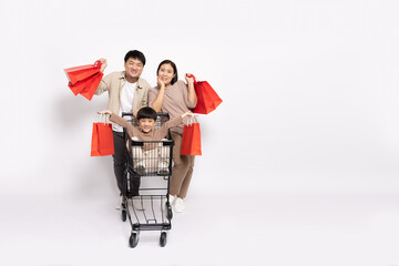 Asian little boy sitting inside of shopping trolley and holding shopping bag and Father and mother pushing shopping cart isolated on white background, Family and shopping mall concept