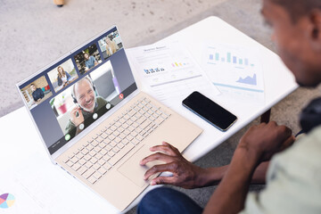 Poster - Multiracial man with cellphone and documents on desk discussing with coworkers on video call
