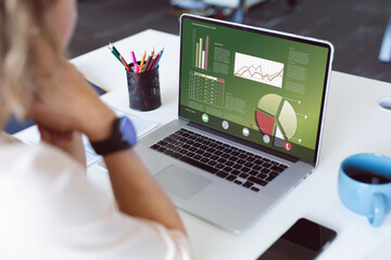 Poster - Caucasian businesswoman analyzing business report over laptop on table at office