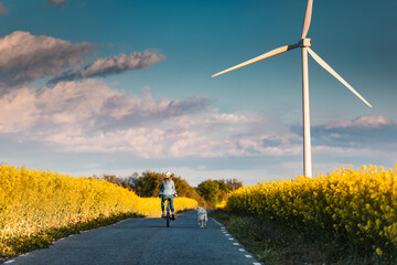 Shot of beautiful young girl riding a bike while walking her dog in the park through rapessed field.