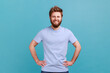© khosrork - Portrait of satisfied happy bearded man standing with hands on hips and looking at camera with toothy smile, having positive confident expression. Indoor studio shot isolated on blue background.