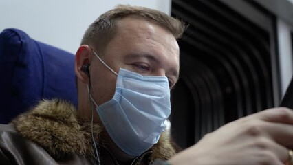 Wall Mural - Millennial man commutes on train looks social media, listens music, texts messages, uses cell phone while riding home by train passes through suburbs during Covid-19 or coronavirus pandemic