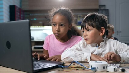 Multiethnic elementary school kids building robots developing program for software robotics engineering using laptop at classroom lab. AI technologies development. STEM education concept. 4k footage