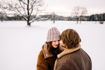 Cute young couple in love having fun in the winter park on bright day. Woman and man relaxing outdoors