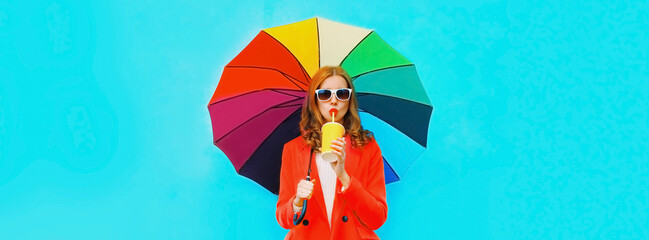 Wall Mural - Autumn portrait of young woman with colorful umbrella drinking juice or cup of coffee wearing red jacket on blue background