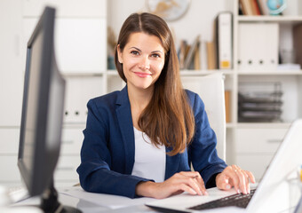 Wall Mural - Portrait of confident smiling female office employee during daily work with laptop and documents