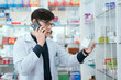 © 2B - A male pharmacist checks drug stocks in a community pharmacy. use the phone to talk