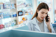© 2B - A female pharmacist checks drug stocks in a community pharmacy. use the phone to talk