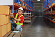 © feeling lucky - Warehouse worker man with saftyhat and reflective jacket checking list or control large box package for delivery to production stock and inventory in retail warehouse logistics, distribution center