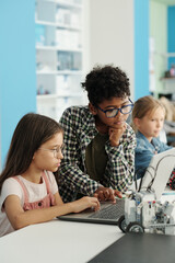 Two youthful schoolkids in casualwear and eyeglasses looking at laptop screen while preparing presentation of new project at lesson