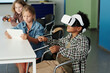 © pressmaster - Side view of cute African American schoolboy in vr headset controling virtual robot while his classmate watching action on tablet screen