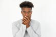 Portrait of African American man covering mouth with hands. Young bearded guy wearing white sweater looking at camera ashamed of bad breath. Silence and halitosis concept