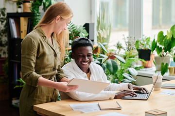 Aufkleber - Happy young African American businessman looking at data shown by blond female colleague consulting with him at meeting
