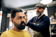 © ADDICTIVE STOCK - Professional Hispanic barber fixing hair of client with spray in barbershop