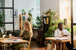 © pressmaster - Two young intercultural designers working in front of computers while sitting by desks in openspace office with many green plants