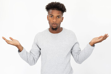 Wall Mural - Portrait of ignorant African American man shrugging shoulders. Young bearded guy wearing white sweater looking at camera in confusion against white background. Ignorance and uncertainly concept