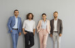 © Studio Romantic - Successful stylish business team standing in studio. Group portrait of four happy confident young people in smart office suits standing together against grey wall, looking at camera and smiling