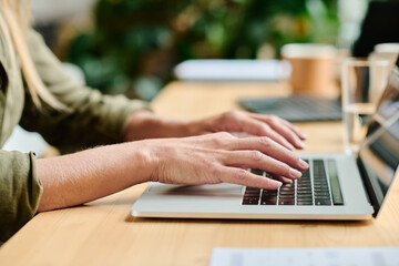 Aufkleber - Side view of hands of young businesswoman typing on laptop keyboard while sitting by table in office or cafe and working over project