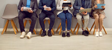 Group Of Diverse People Using Different Laptop And Tablet Computers While Sitting In Line And Waiting For Business Meeting Or Job Interview. Legs, Feet On Office Floor, Crop Low Section Shot. Banner