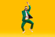 Cheerful energetic man has fun dancing in gangnam style at St. Patrick's Day party. Full length of man in trendy green suit and sunglasses of same color doing funny dance moves on orange background.