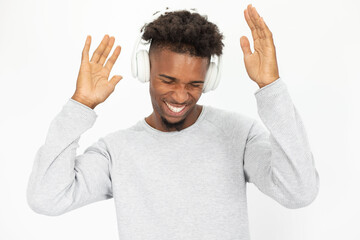 Wall Mural - Portrait of joyful African American man listening to music in headphones. Young bearded guy wearing white sweater dancing to music against white background. Hobby and music concept