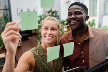 Aufkleber - Young smiling blond female employee explaining her colleague working points written on notepapers on transparent noticeboard