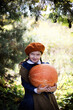 Dziewczynka w berecie i jesiennych barwach trzyma wielką dynię