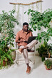 © pressmaster - Young serious African American businessman in casualwear using laptop while networking or watching online video among green plants