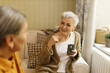 © shurkin_son - Stylish Caucasian retired female in warm cardigan holding mug looking at her unrecognizable female friend having curious facial expression, listening attentively. Two elderly women talking