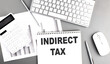 INDIRECT TAX text written on notebook on grey background with chart and keyboard, business concept