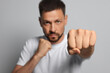 © New Africa - Man throwing punch against grey background, focus on fist. Space for text
